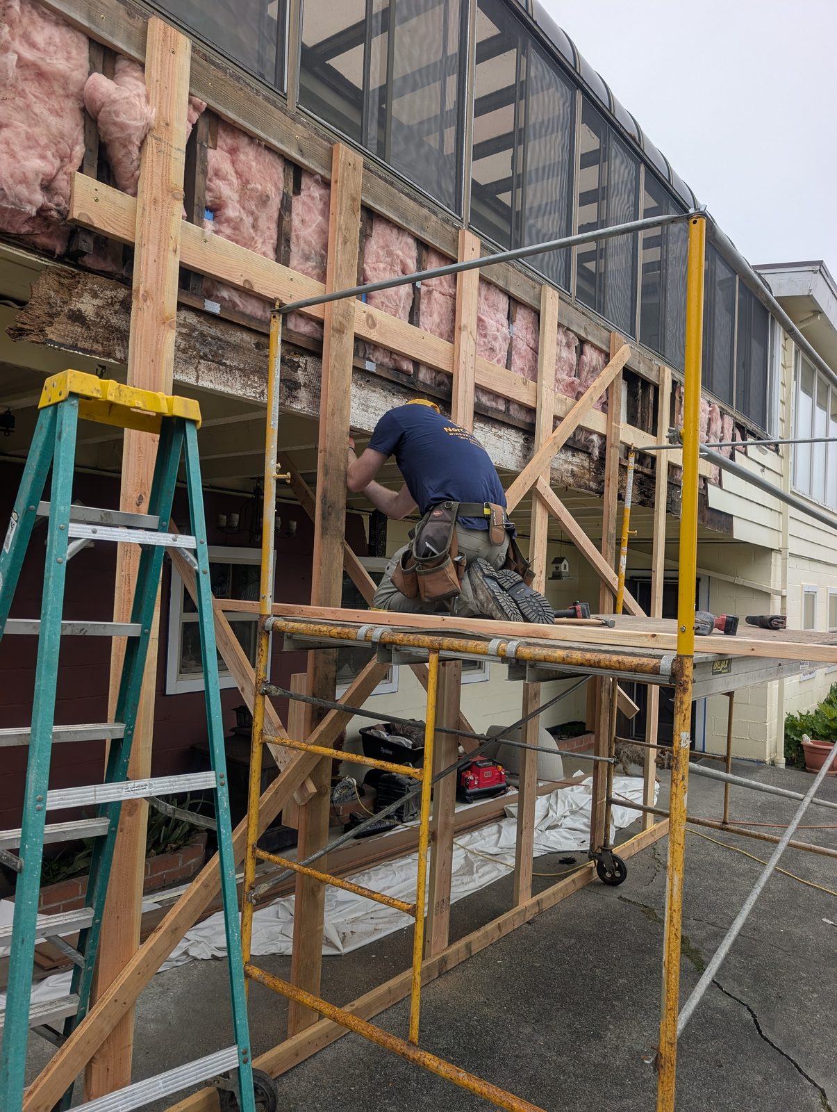 NorCal Exterior crew member rebuilding wall framing on scaffolding during a major siding repair project, sister joists and fresh insulation visible